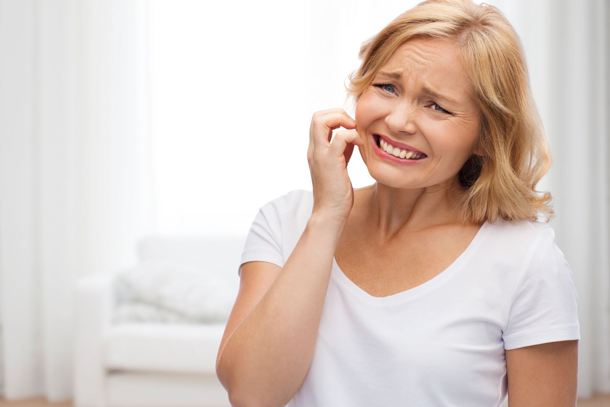 A woman in a white shirt scratching her face wondering, “Why does my acne itch?”