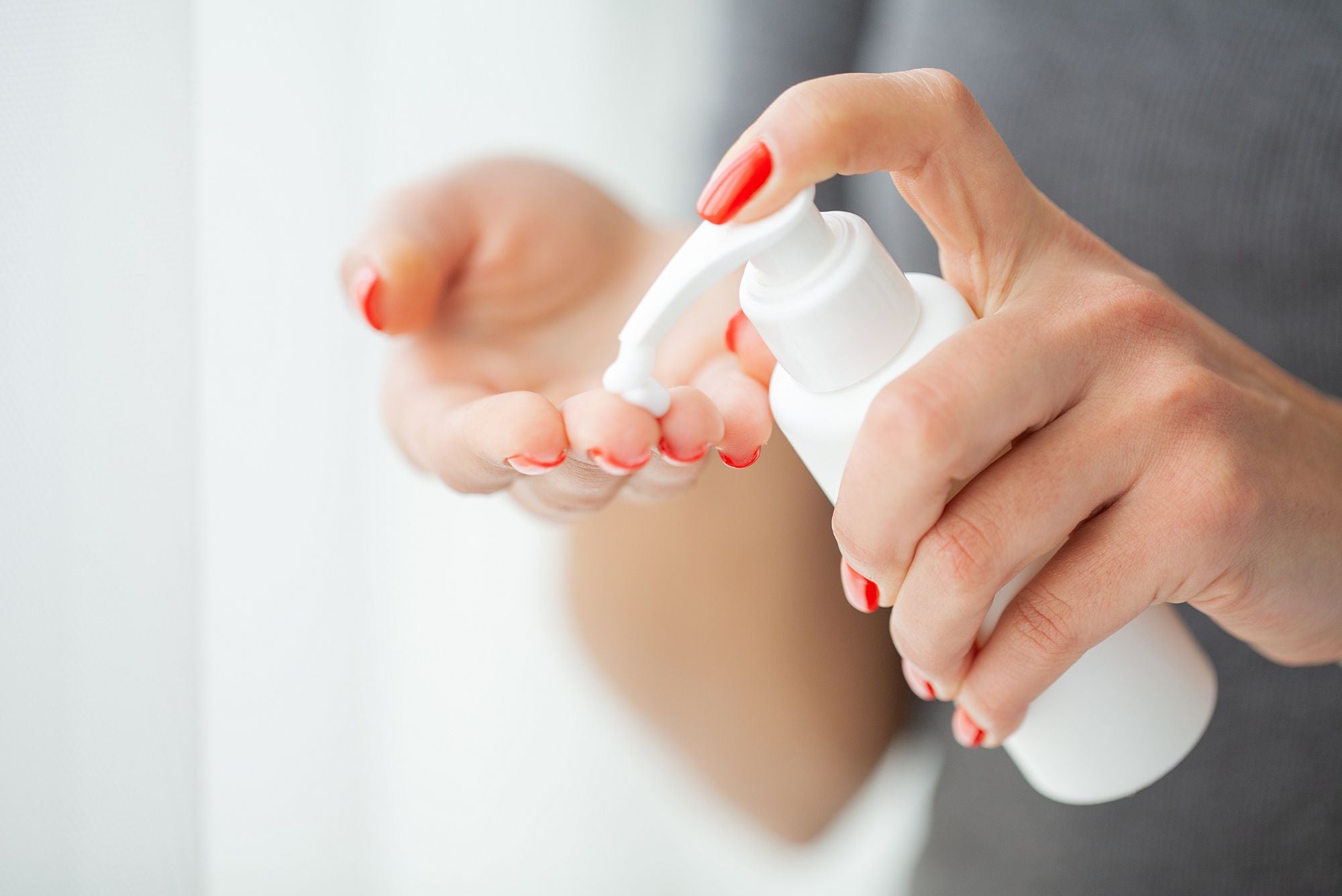 A woman with red fingernails dispenses her moisturizer while asking herself, "Does moisturizer cause acne?"