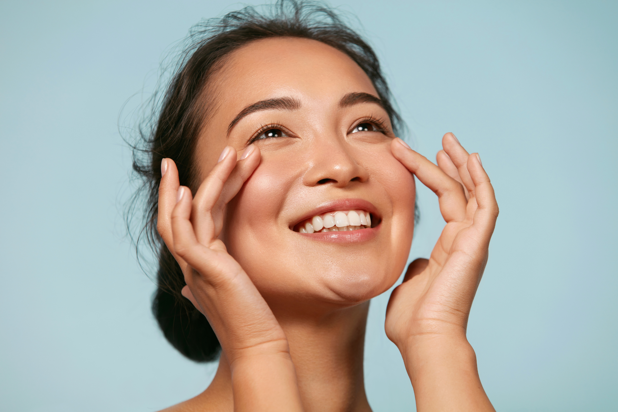 A woman smiles while rubbing in a red light therapy skin care product after treatment.