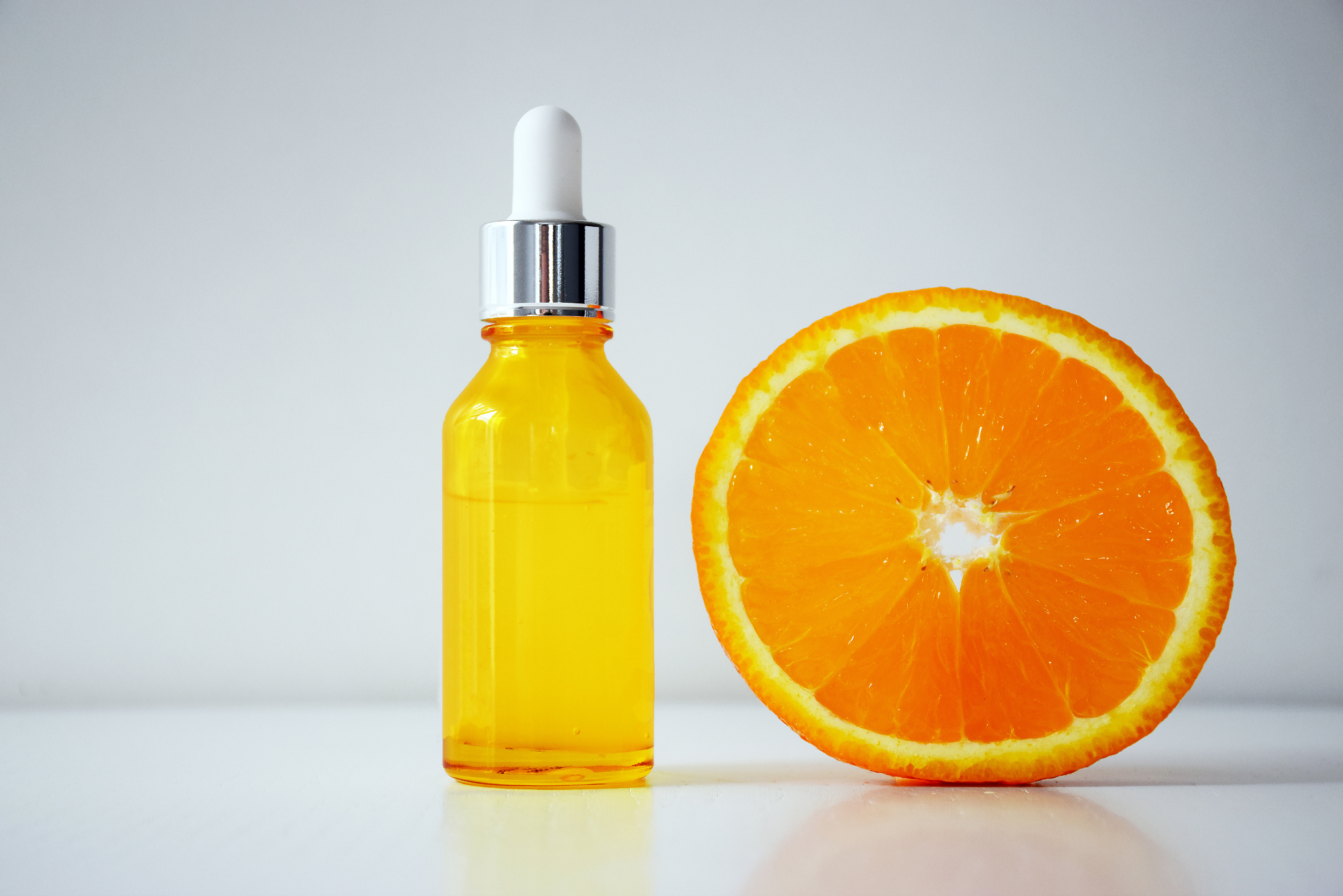 A bottle of serum next to an orange slice represents the relationship between vitamin C serum and red light therapy.