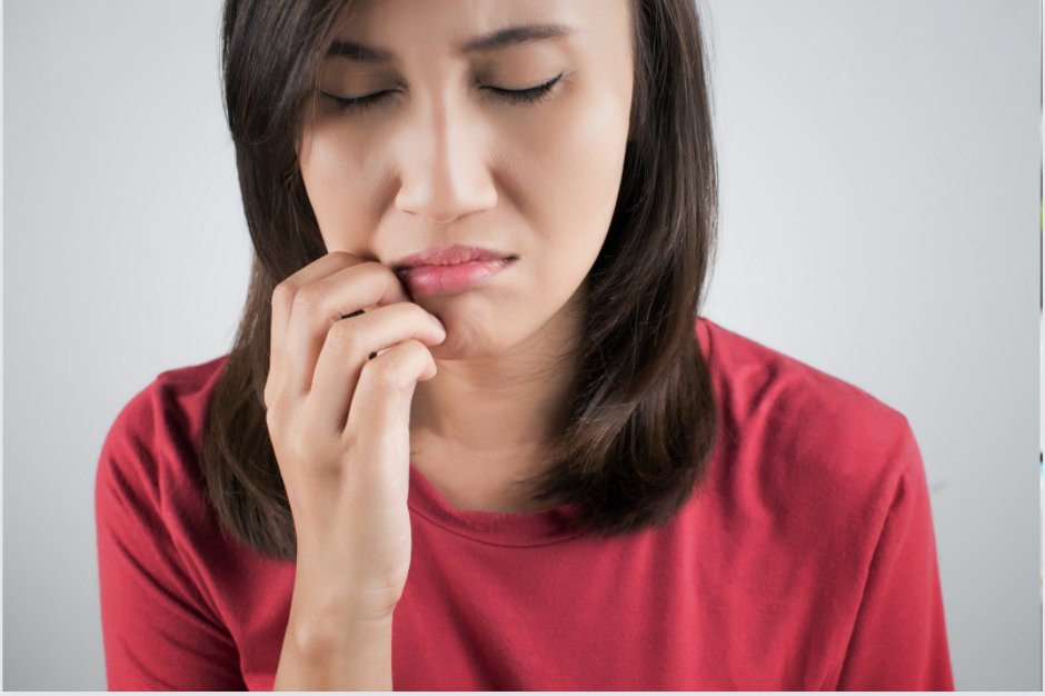 A woman in a red shirt closes her eyes and holds her lip in pain because of a canker sore.